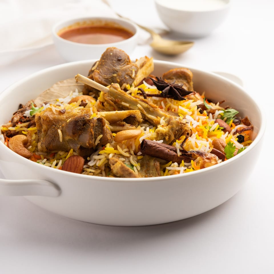 Close-up of a white bowl filled with Curry Nights Indian Cuisine's lamb biryani, garnished with nuts and spices.