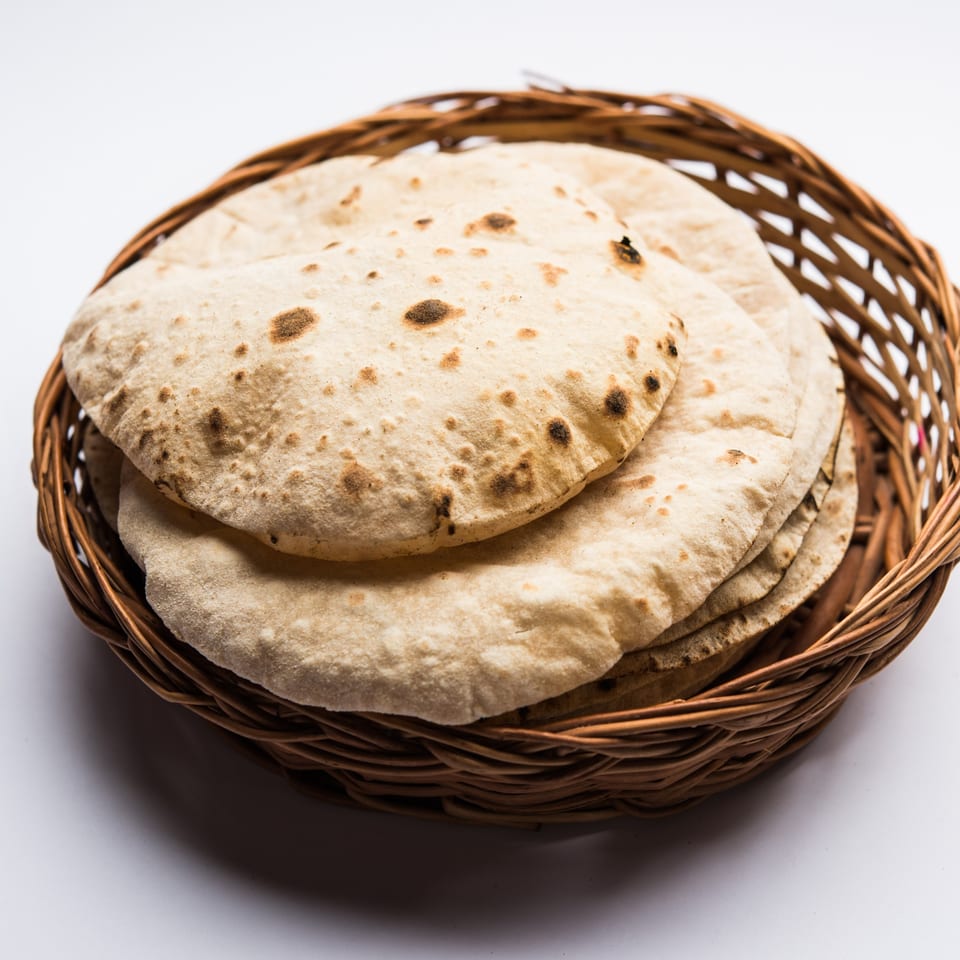 A woven basket filled with several round, lightly browned Indian flatbreads, likely from Curry Nights.