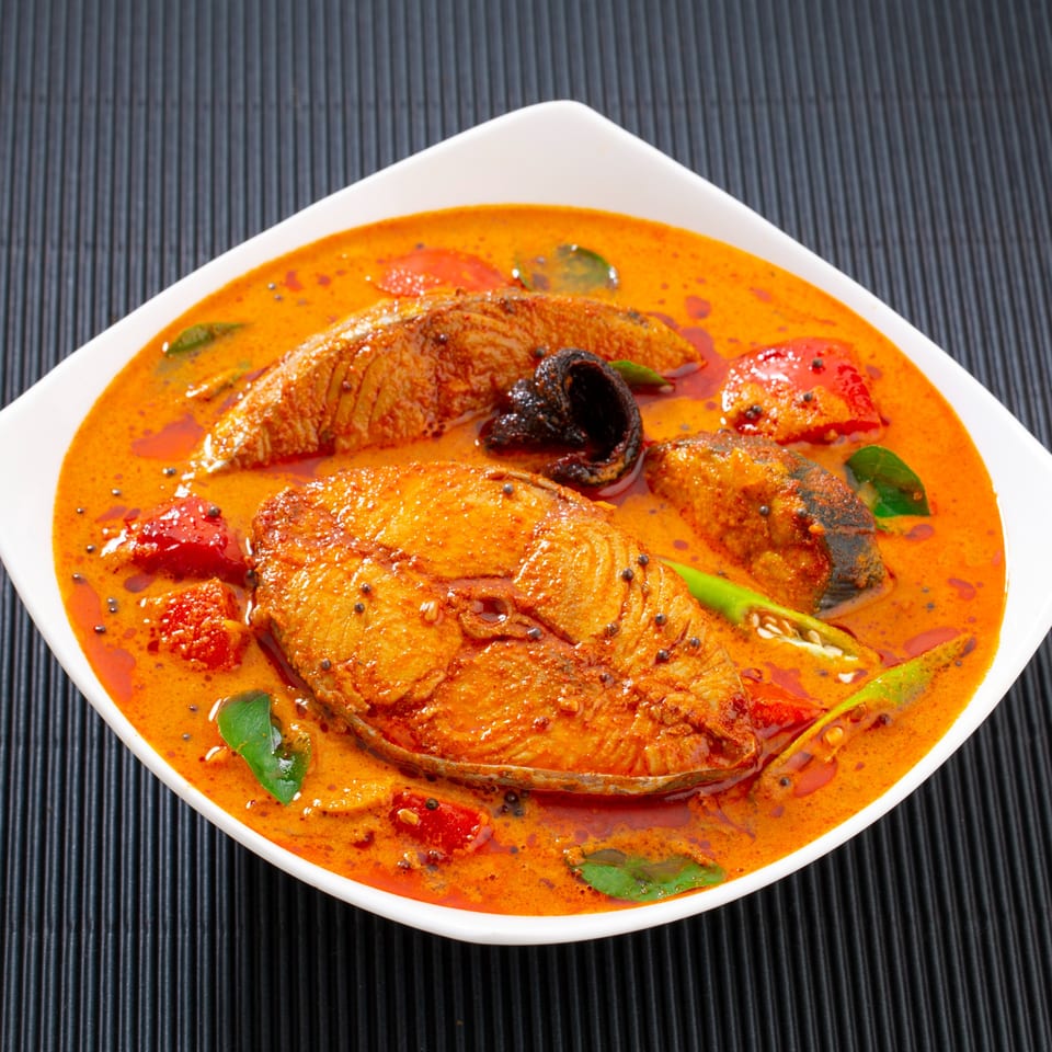 Indian fish curry with red chili, green peppers, and curry leaves in a white bowl.